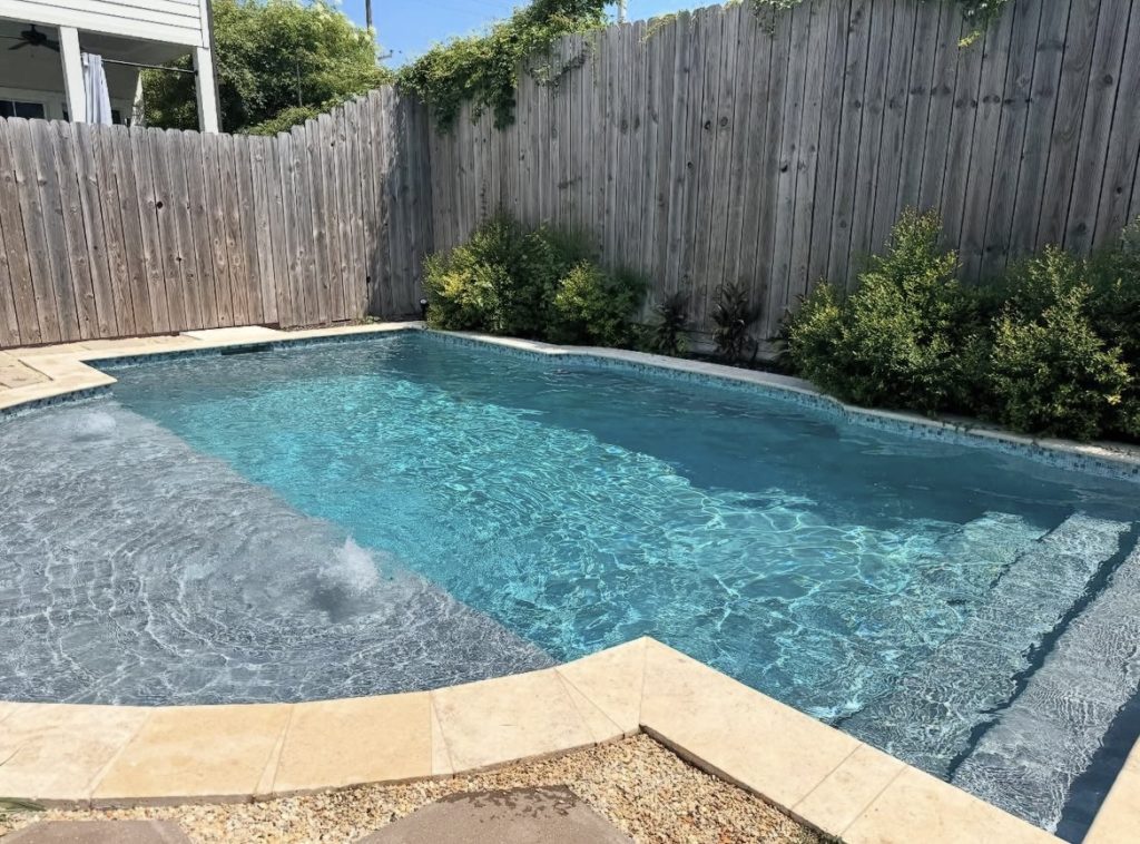 Freshly serviced backyard pool with clear blue water and travertine coping