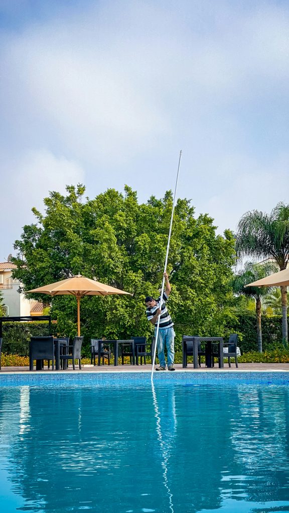 Pool technician skimming leaves from a backyard swimming pool