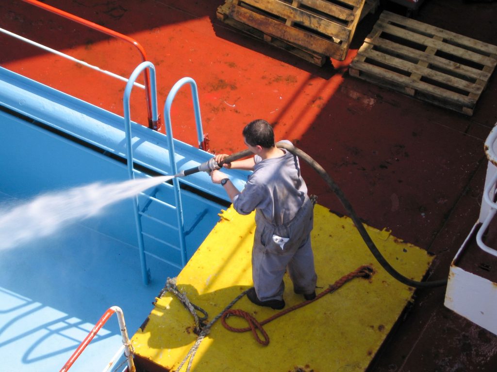 Technician pressure-washing the walls of a drained pool